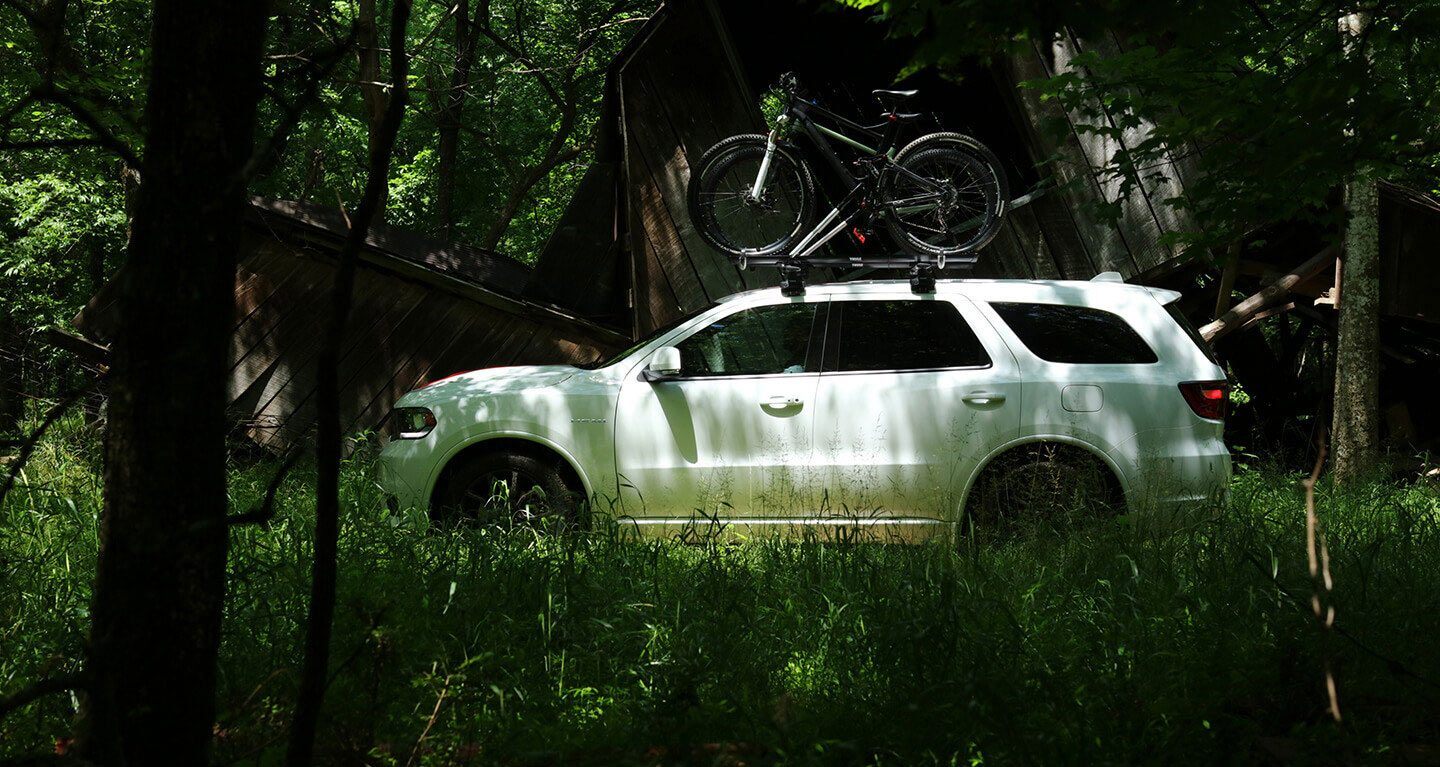 Mostrar: Vista del perfil de un Dodge Durango 2020 estacionado en un bosque con dos bicicletas atadas a la parrilla portaequipajes.