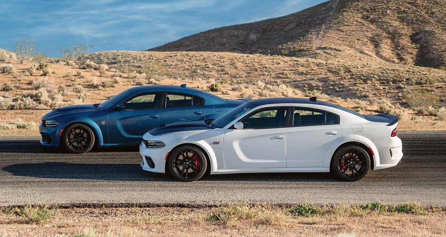 Dos modelos Dodge Charger 2020 aparcados en un camino desierto.