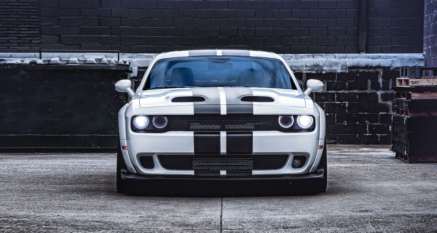 Toma frontal de un Dodge Challenger SRT Hellcat Redeye Widebody 2022 blanco delante de una pared de ladrillos negros.