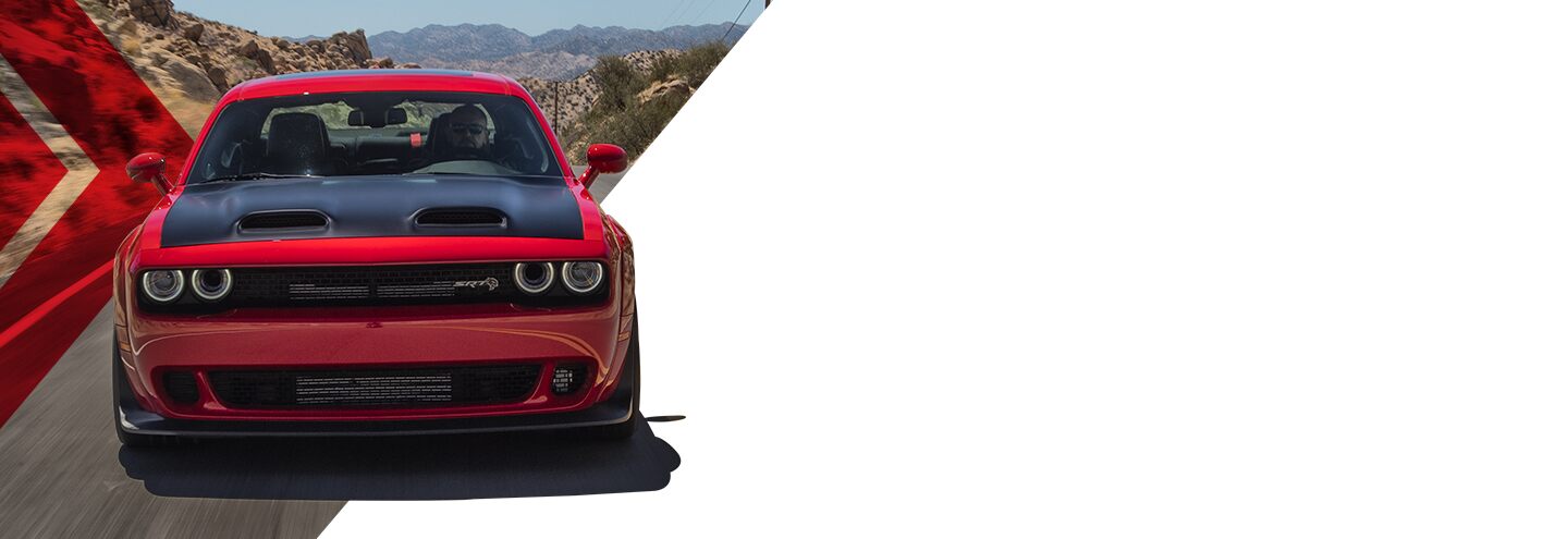 Un ángulo delantero de un Dodge Challenger SRT Hellcat 2023 rojo con un capó negro andando por una carretera por las montañas.