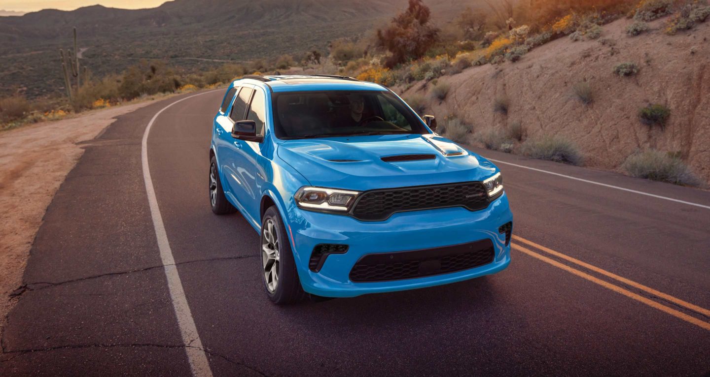 Se muestra: un Dodge Durango GT HEMI 2026 azul circulando por una carretera sinuosa en las montañas.