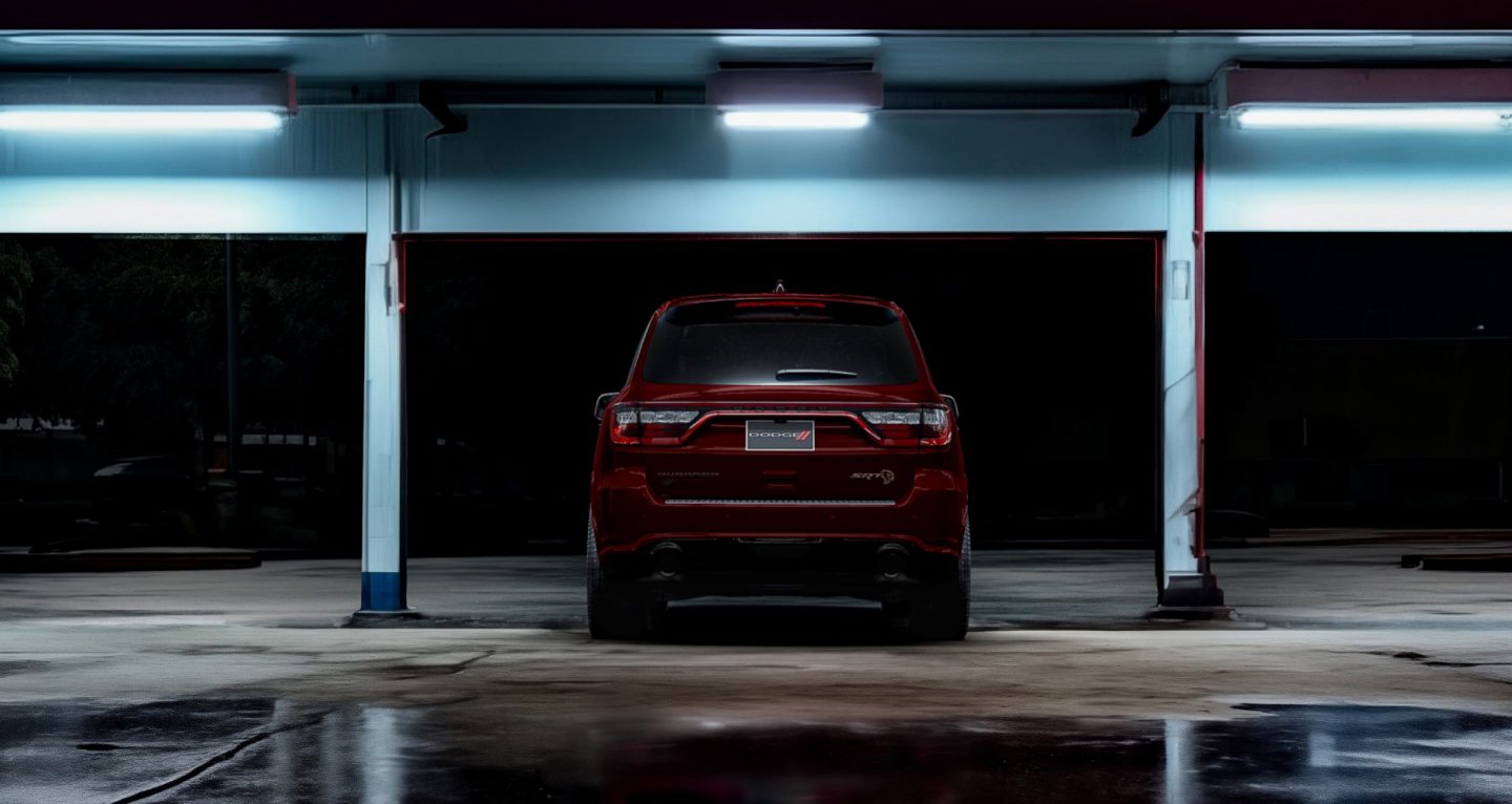 Se muestra: una vista trasera de un Dodge Durango SRT Hellcat 2026 rojo en una estructura de estacionamiento iluminada.