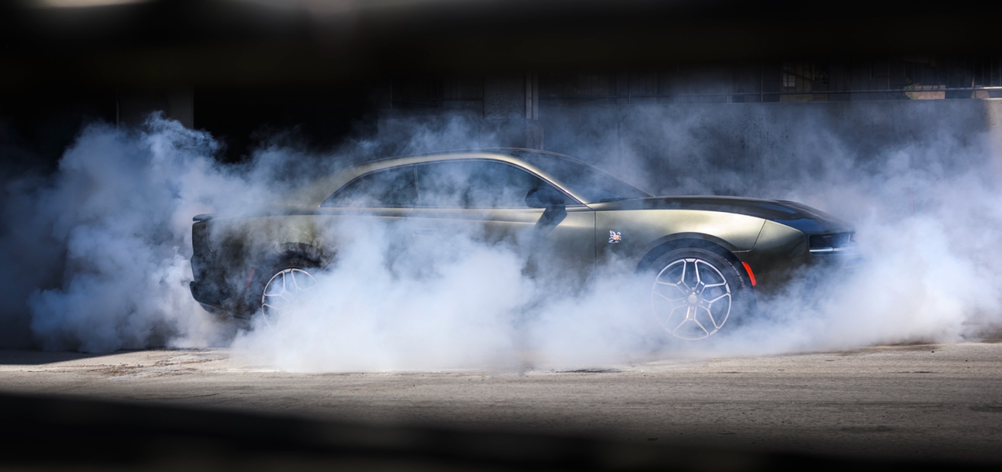 A silver 2027 Dodge Charger Scat Pack in profile, with smoke surrounding the car.