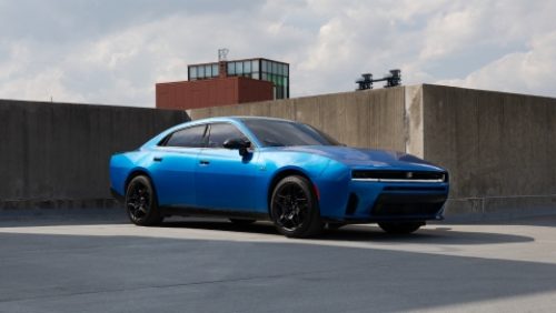 Un Dodge Charger Scat Pack 2027 azul tomando una curva en una carretera rural.