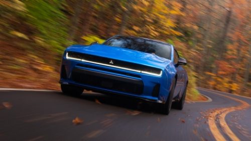 A blue 2027 Dodge Charger Scat Pack taking a curve on a country road.