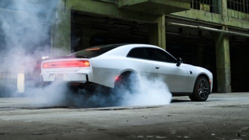 A white 2027 Dodge Charger Scat Pack, with smoke coming from its rear tires, shot from a rear profile.