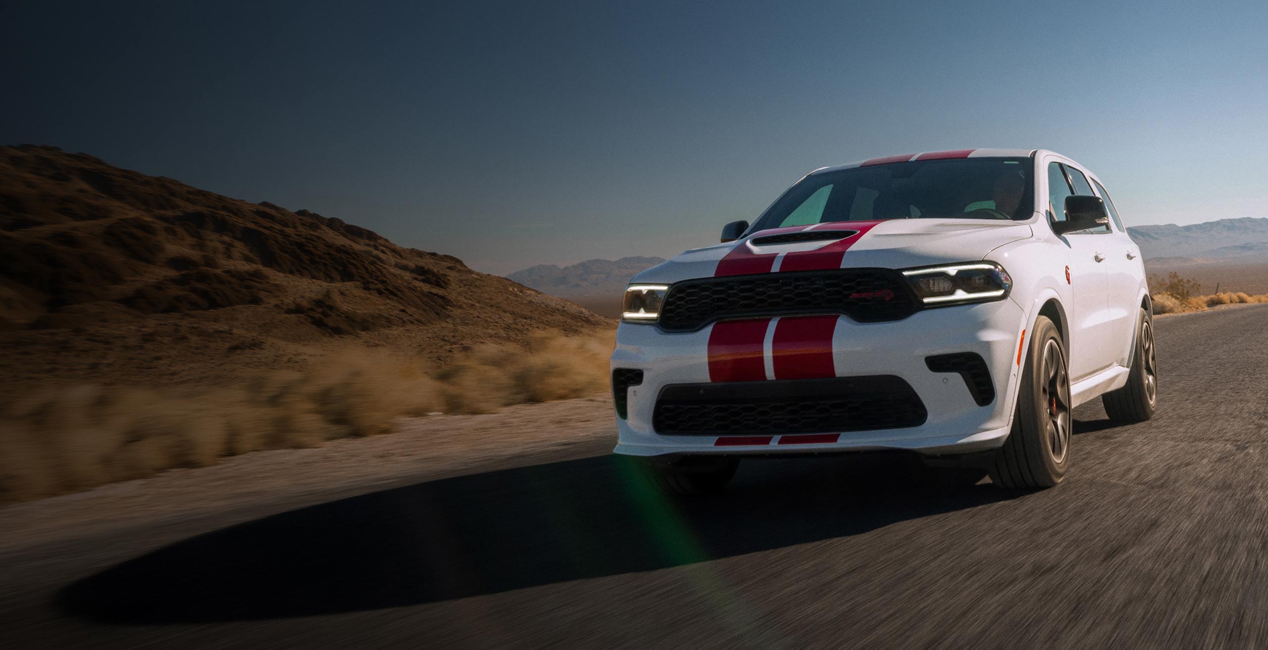 A Dodge Durango in White Knuckle driving on a desolate road with a hill in the background.