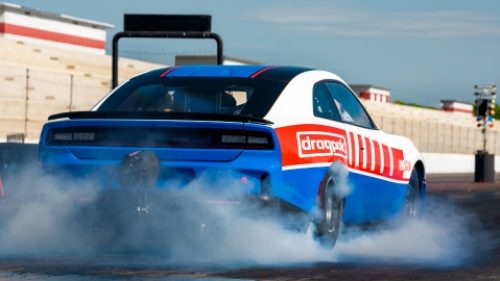 El lado del conductor de un Dodge Charger Scat Pack 2027 verde oliva, estacionado en un garaje industrial.