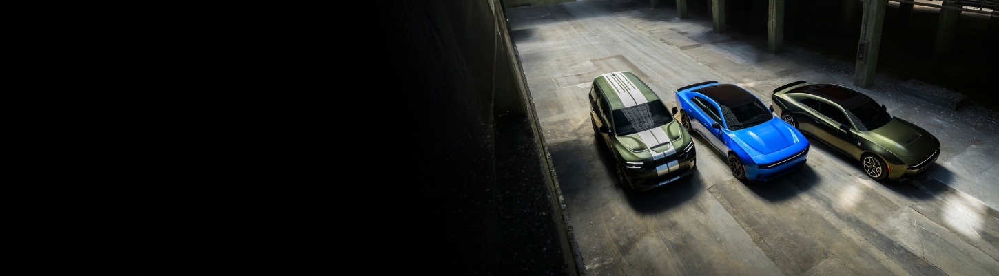 An overhead angle of a green 2026 Dodge Durango SRT Hellcat Jailbreak with dual white center stripes, a blue 2026 Dodge Charger Scat Pack with black roof and a green 2026 Dodge Charger Scat Pack Plus parked near each other.