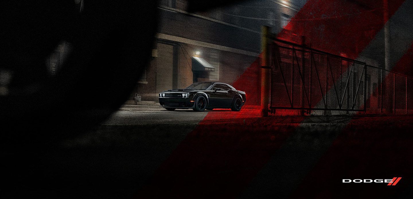 Un Dodge Challenger SRT Hellcat Widebody 2021 negro estacionado en un callejón, de noche, con las franjas deportivas Dodge rojas superpuestas en el fondo.
